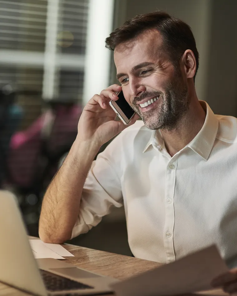 Homem em momento tranquilo de trabalho, ao telefone e sorrindo