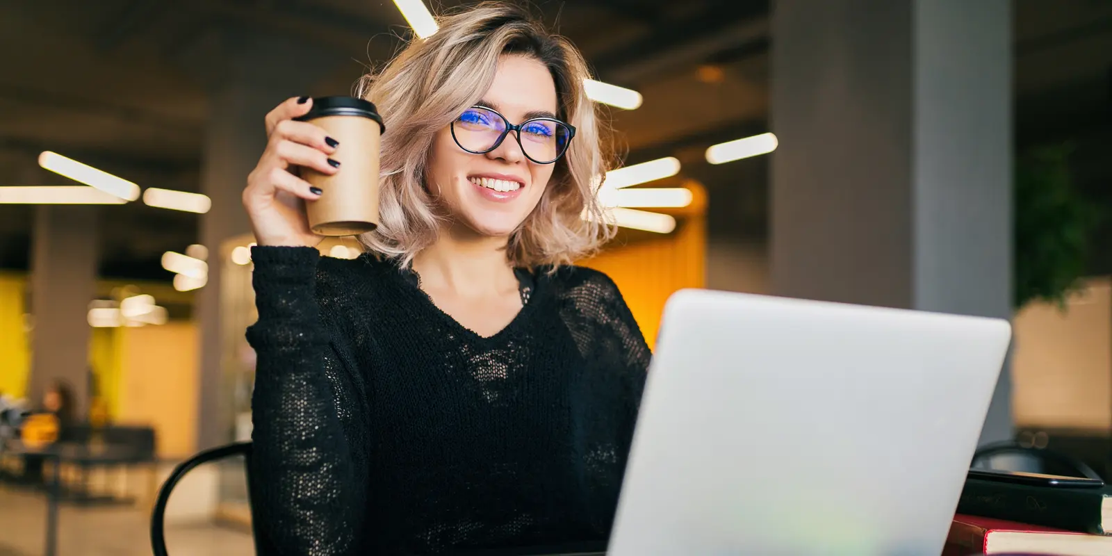 Mulher em momento de bem-estar no trabalho, sorrindo com café